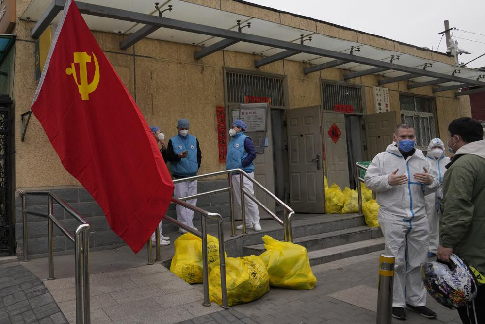 Community workers outside a locked down community chat near a Communist Party flag and trash bags labelled as hazardous waste on Thursday, March 17, 2022, in Beijing.