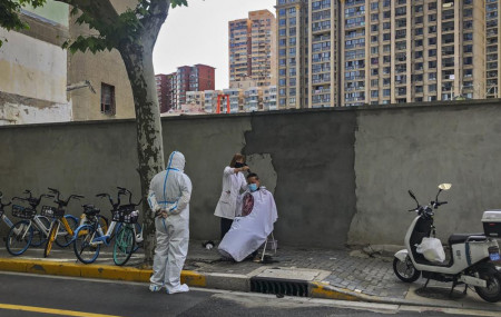 A worker in protective gear watches a barber cuts a resident's hair Tuesday, May 31, 2022, in Shanghai, China.