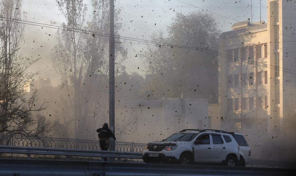 A police officer watches stone and earth debris flying through the air as Russian kamikaze drones hit the centre of the capital Kyiv, Ukraine, Monday, Oct 17, 2022. (AP/RSS Photo)