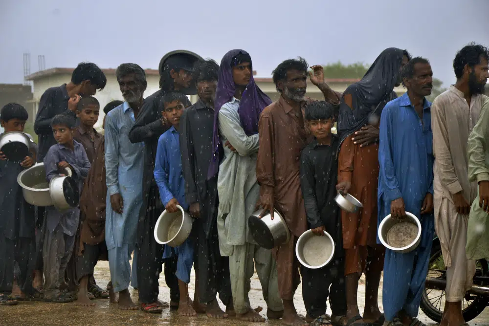 People wait in the rain for their turn to receive free food distributed by volunteers outside a camp of internally displaced people from coastal areas in Sujawal, Pakistan's southern district in the Sindh province, Thursday, June 15, 2023, as Cyclone Biparjoy was approaching.  AP/RSS Photo